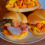 Pan con chicharrón peruano: crujientes chicharrones de cerdo sobre pan francés, camote frito y salsa criolla.