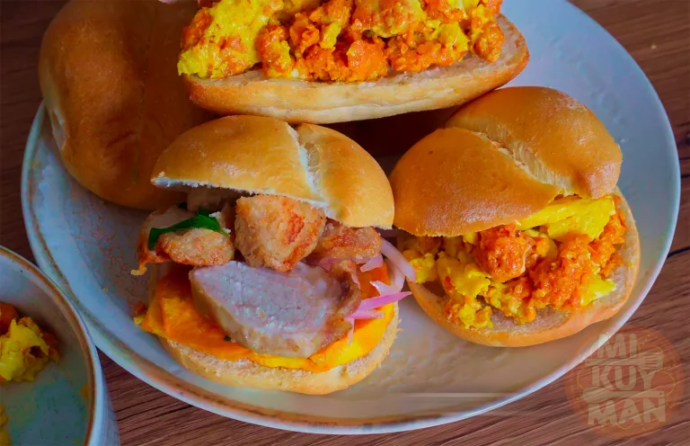 Pan con chicharrón peruano: crujientes chicharrones de cerdo sobre pan francés, camote frito y salsa criolla.