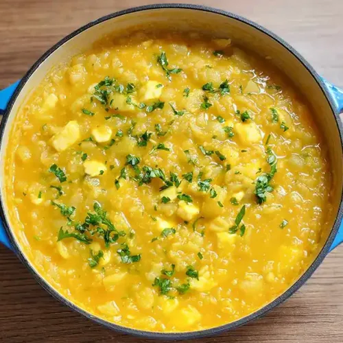 Ajiaco de olluco cremoso y caliente servido en un plato, con perejil picado y queso fresco.