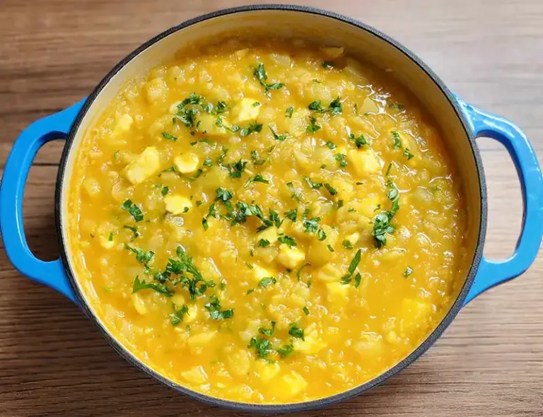 Ajiaco de olluco cremoso y caliente servido en un plato, con perejil picado y queso fresco.