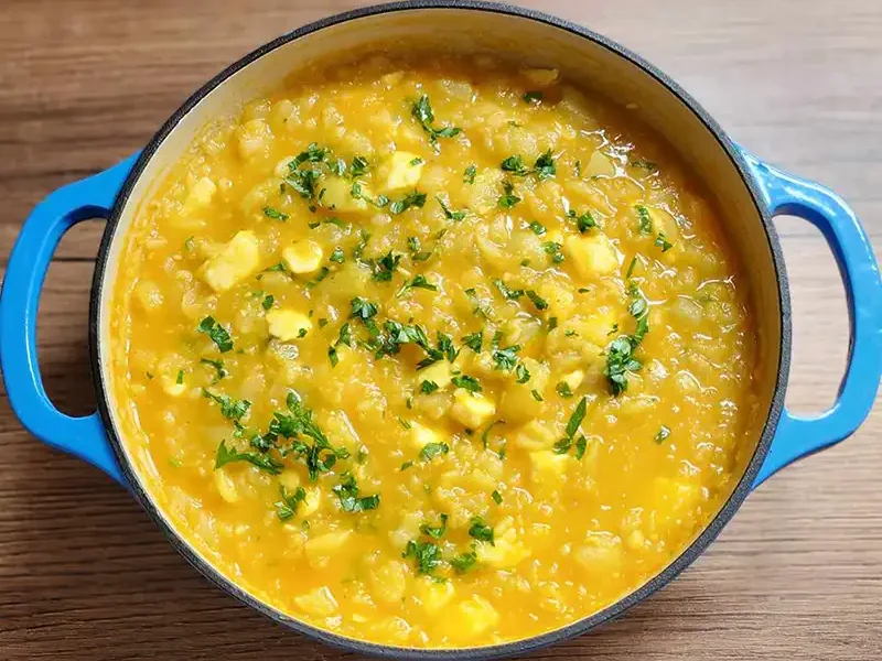 Ajiaco de olluco cremoso y caliente servido en un plato, con perejil picado y queso fresco.