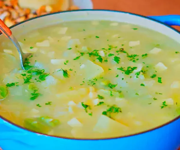 Plato hondo con sopa de calabaza cremosa, decorado con queso fresco y perejil, sobre una mesa rústica.
