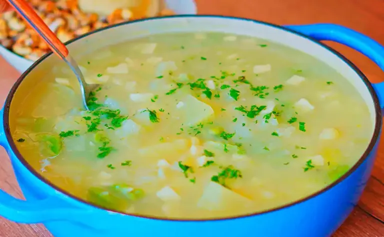Plato hondo con sopa de calabaza cremosa, decorado con queso fresco y perejil, sobre una mesa rústica.