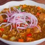 Deliciosas lentejas peruanas con pollo, acompañadas de vegetales frescos en un plato colorido.