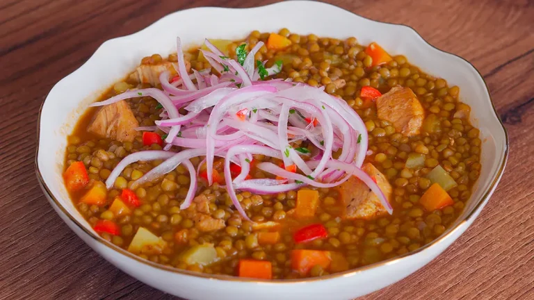 Deliciosas lentejas peruanas con pollo, acompañadas de vegetales frescos en un plato colorido.