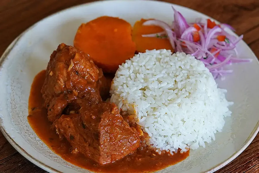 Adobo de chancho arequipeño servido en plato de barro con pan serrano y papas sancochadas.