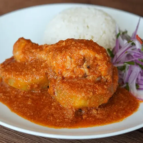 Plato de Pollo al Maní peruano con salsa cremosa, arroz blanco y ensalada de cebolla