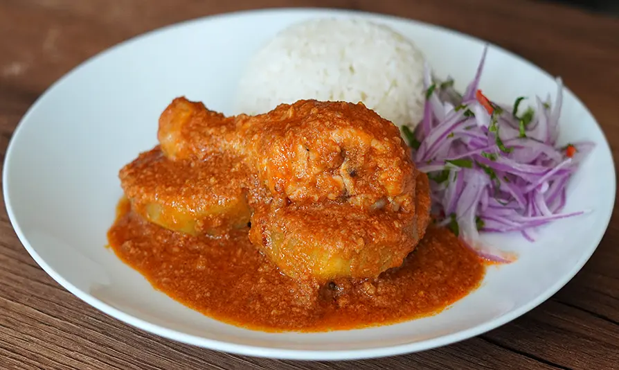 Plato de Pollo al Maní peruano con salsa cremosa, arroz blanco y ensalada de cebolla