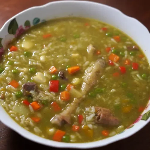 Aguadito de pollo peruano: sopa verde con arroz, arvejas, choclo y una presa de pollo, servida con limón.