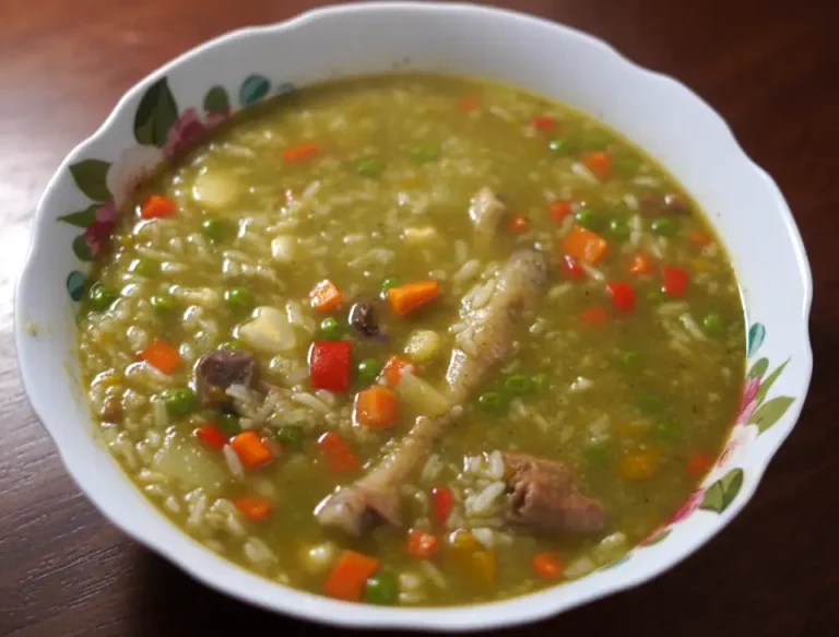 Aguadito de pollo peruano: sopa verde con arroz, arvejas, choclo y una presa de pollo, servida con limón.