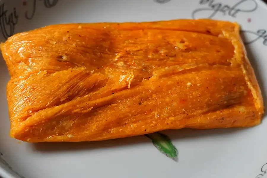 Tamales peruanos tradicionales de maíz rellenos de pollo, aceituna y huevo, envueltos en hojas de plátano.