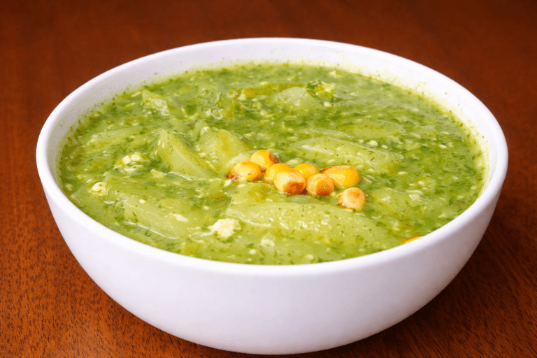 Sopa Verde peruana tradicional con papas, queso fresco y hierbas andinas en cuenco blanco sobre mesa de madera rústica.